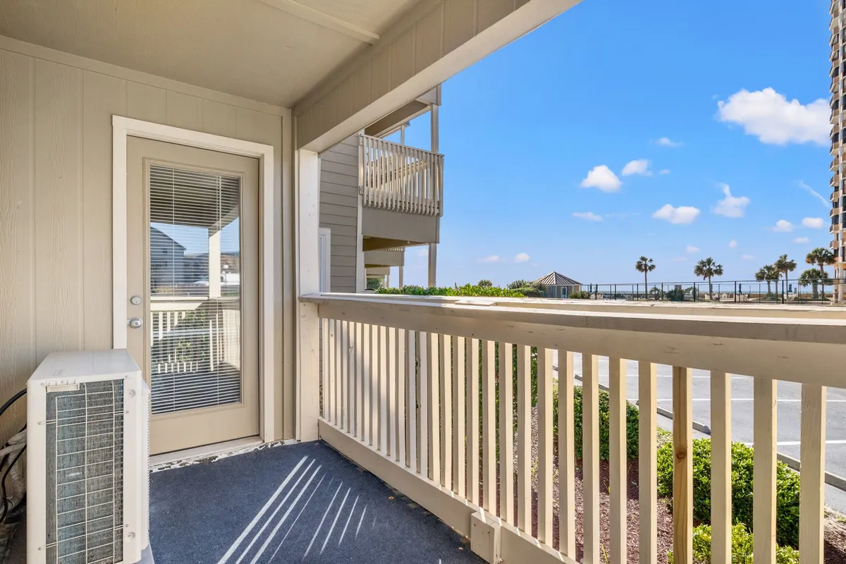 An exterior balcony with a view of the beach, featuring balcony railing, a door leading inside, and an air conditioning unit. The tranquil setting invites relaxation with opportunities to enjoy a morning coffee, read, or watch the sunset over the ocean.