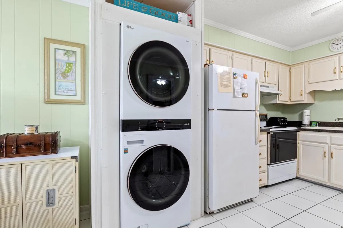 A practical view of the kitchen area, including a stacked washer and dryer, white refrigerator, and black stove. The inclusion of laundry appliances adds a layer of convenience, while the scene suggests a space where families and groups gather to prepare meals and handle daily chores.