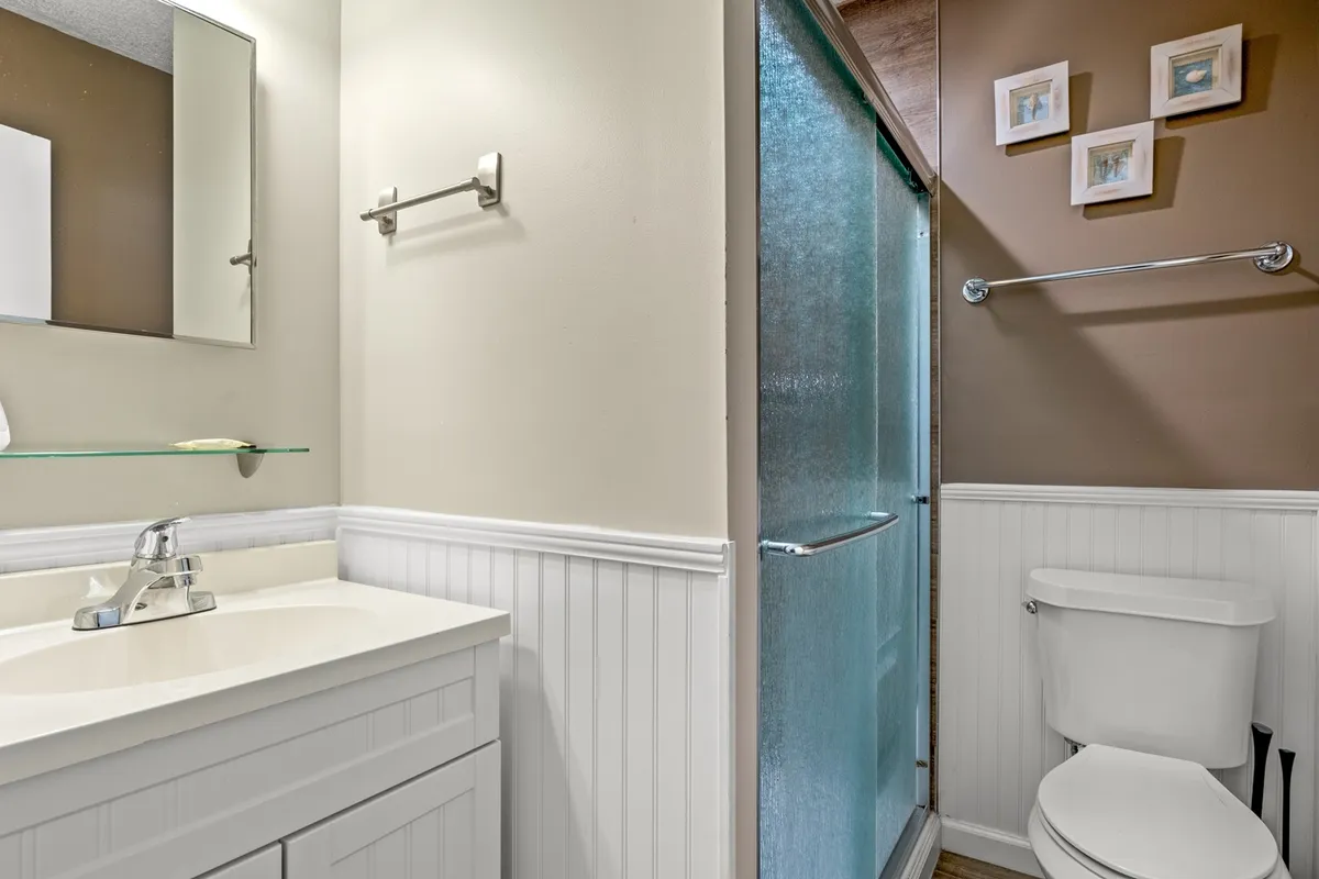 A modern, well-lit bathroom featuring a vanity with a clean sink, a glass-enclosed shower, toilet, and tasteful framed pictures. The area feels refreshing, clean, and perfectly suited for easy morning or evening routines.