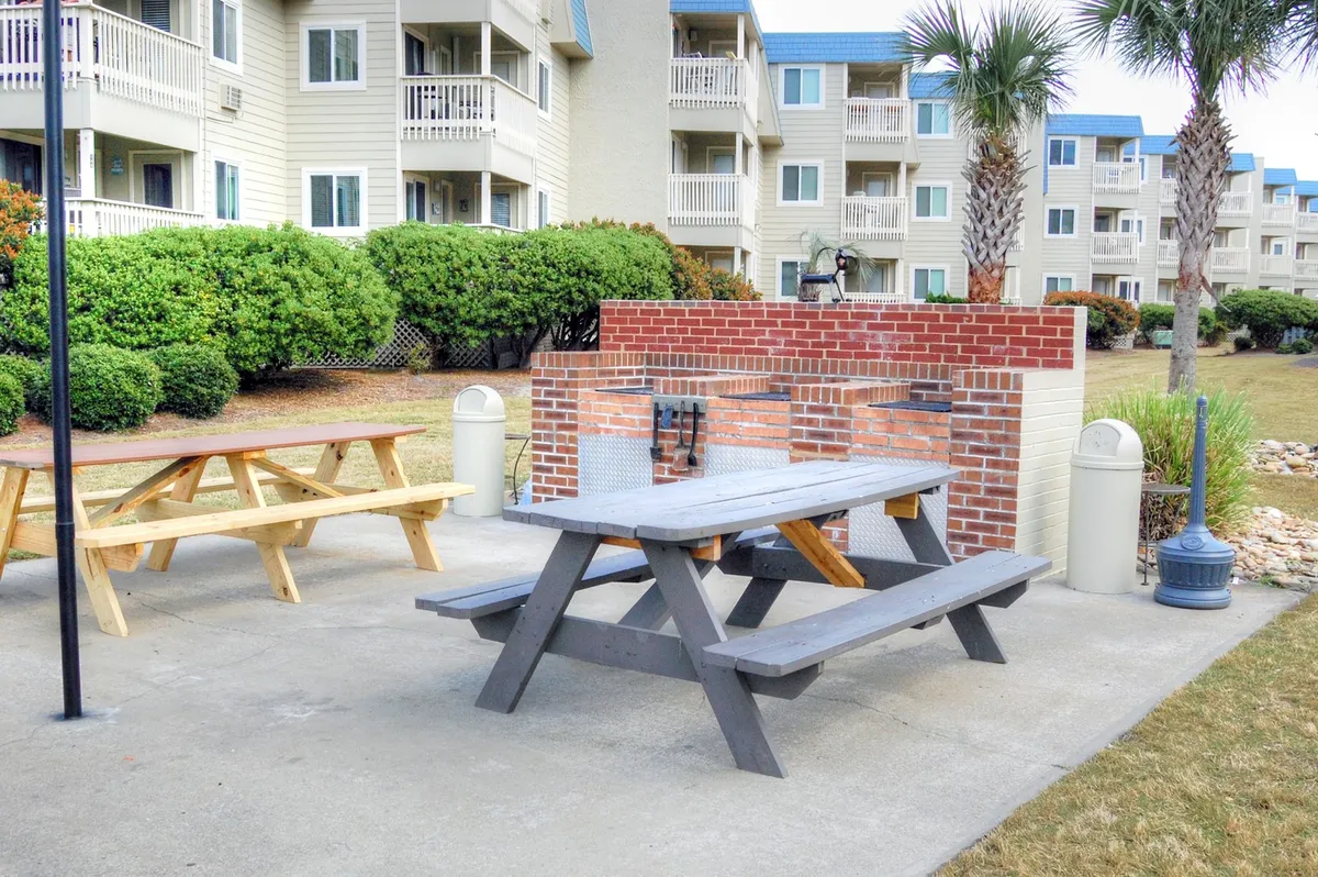 A dedicated grilling area with a picnic table nestled among palm trees and lush greenery. The setup is ideal for outdoor dining, social gatherings, and casual afternoons spent enjoying the Carolina sun with friends or family.