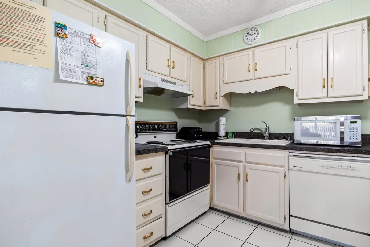 This image captures the main kitchen area, featuring a white refrigerator, black stove, microwave, and kitchen cabinets. The arrangement showcases modern appliances and ample workspace, inviting guests to cook and gather. The scene is active and homey, hinting at meal preparation and socializing.